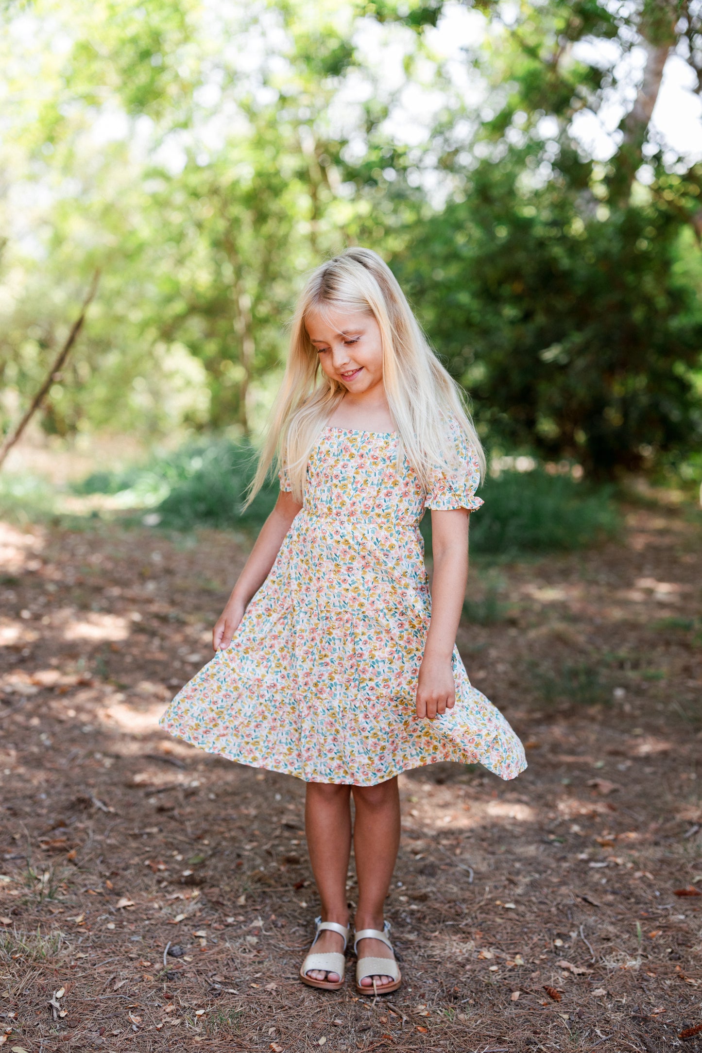 Young girl modeling floral dress standing in a forested area