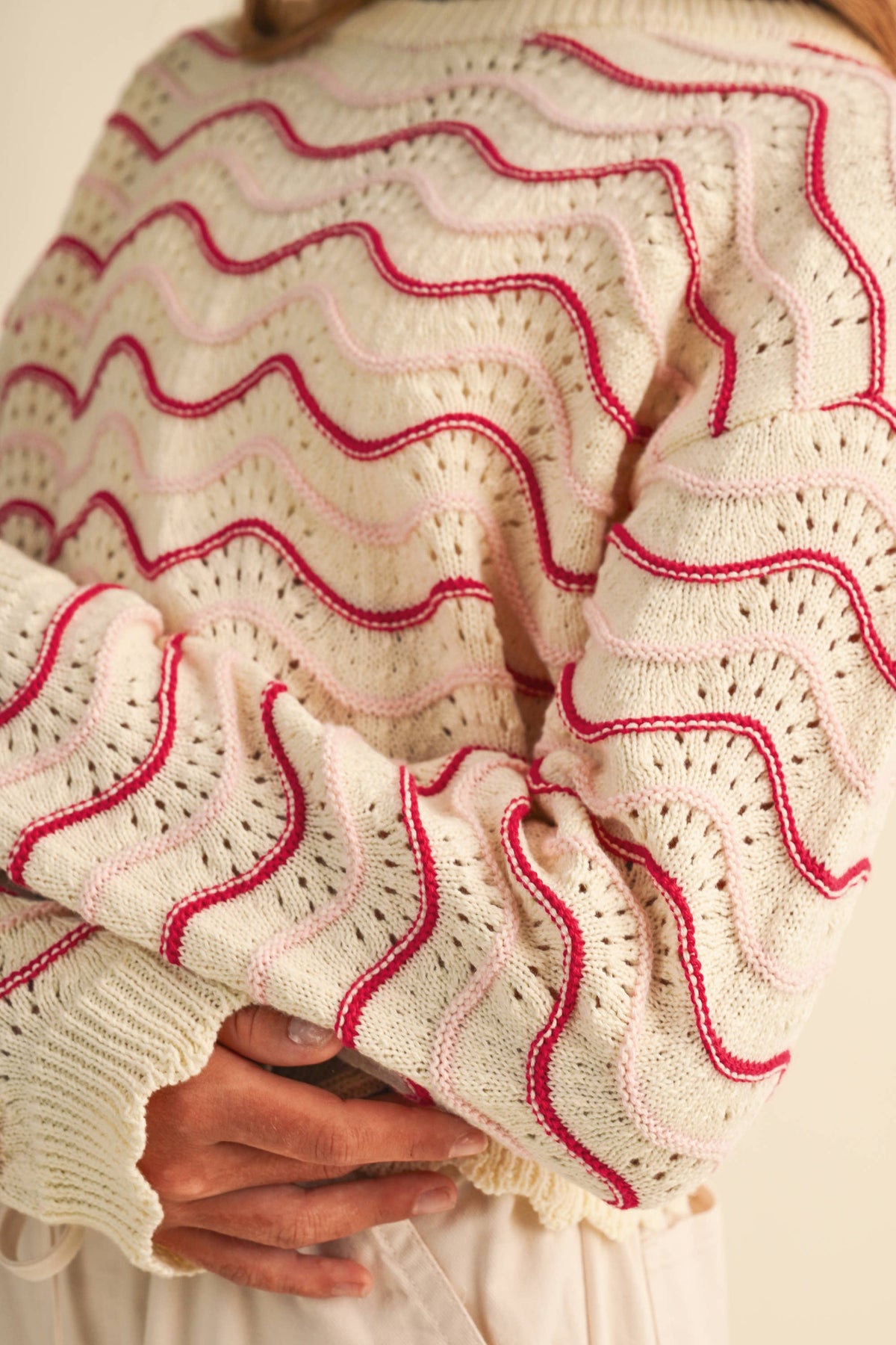 Close-up of a cream-colored knit sweater with wavy pink and red striped patterns