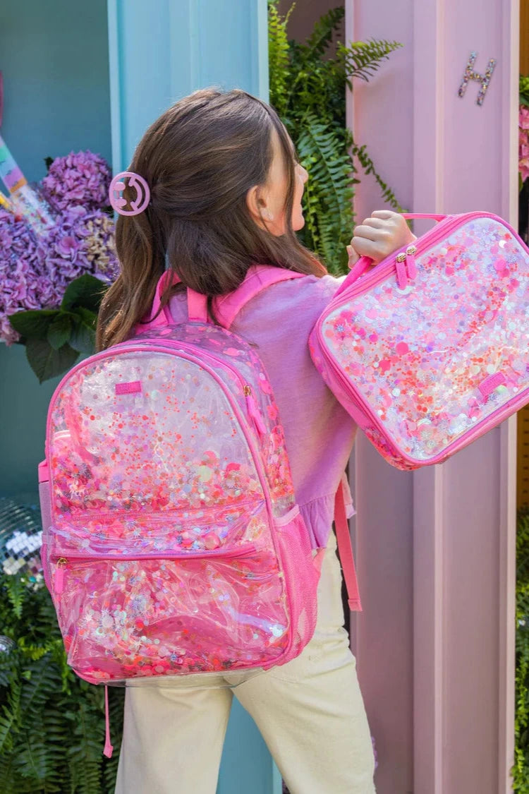 Child holding a pink floral backpack and matching pouch in front of a colorful background