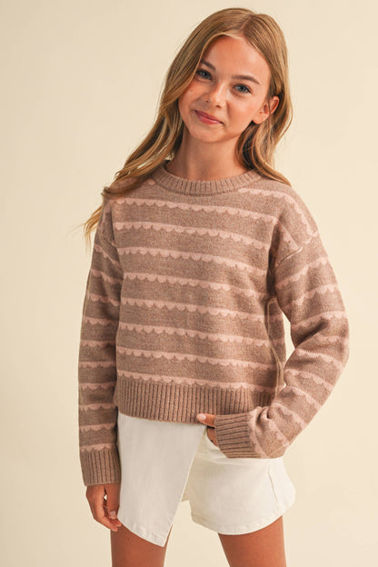 A young girl with blonde hair wearing a brown and beige patterned knit sweater 