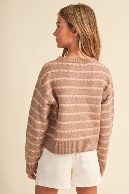A girl shown from the back wearing a cropped knit sweater with horizontal taupe and light pink stripes