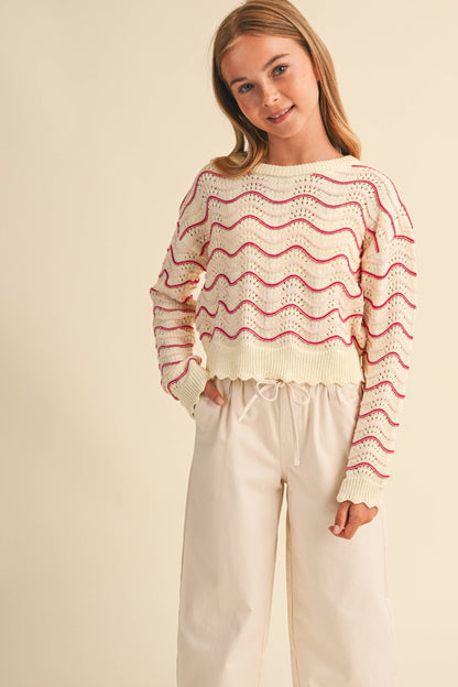 A young girl wearing a cream knit sweater with pink wavy stripes