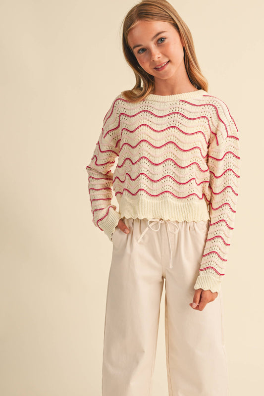 A young girl wearing a cream knit sweater with pink wavy stripes