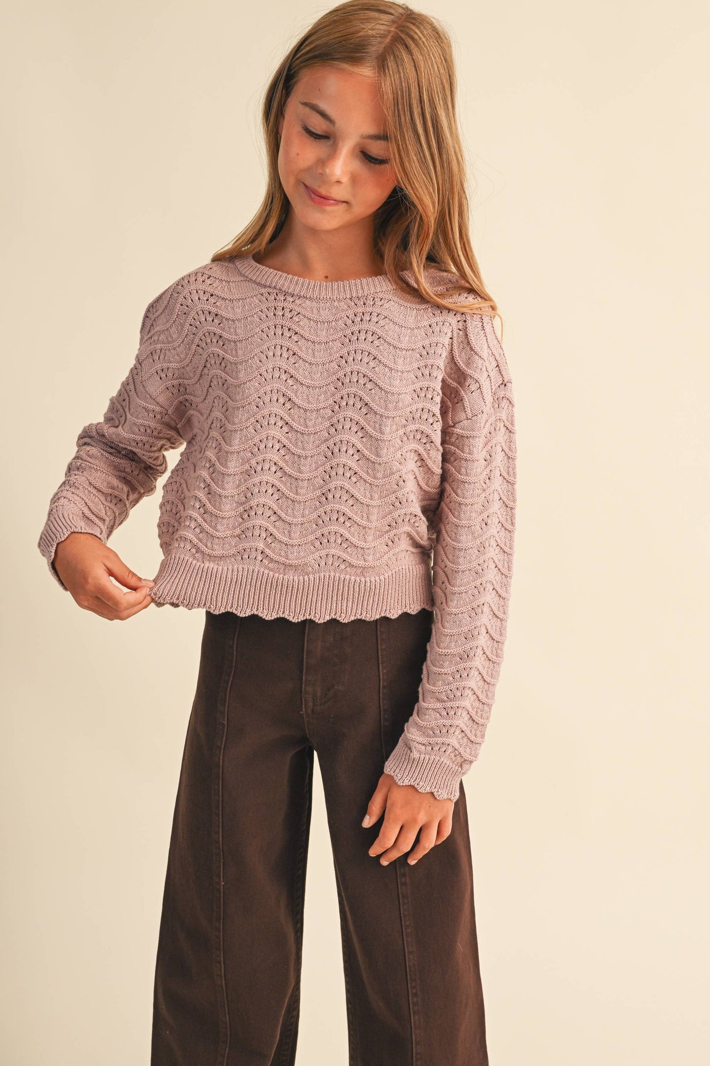 A young girl wearing a dusty pink cable-knit cropped sweater