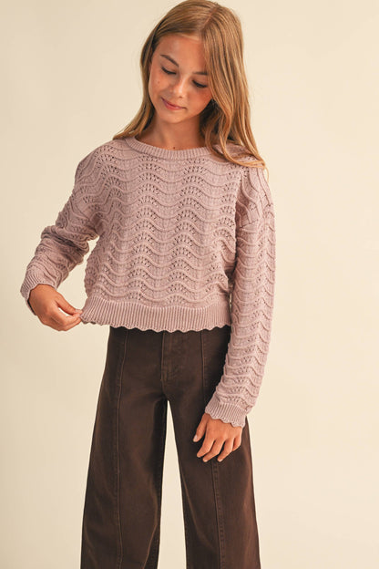 A young girl wearing a dusty pink cable-knit cropped sweater