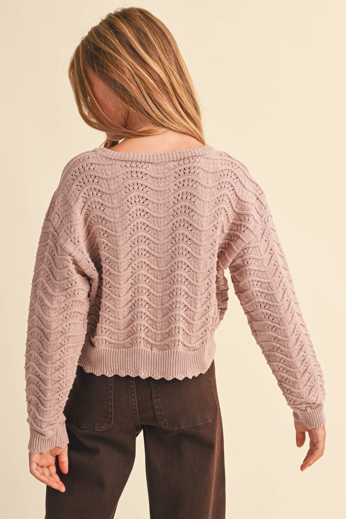 A girl shown from the back wearing a dusty pink textured knit sweater with a wavy chevron pattern 