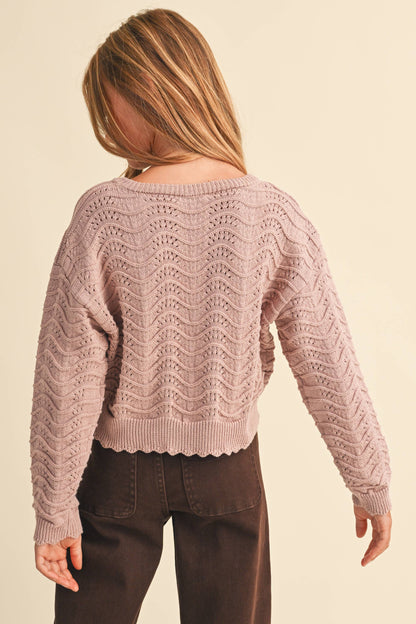 A girl shown from the back wearing a dusty pink textured knit sweater with a wavy chevron pattern 