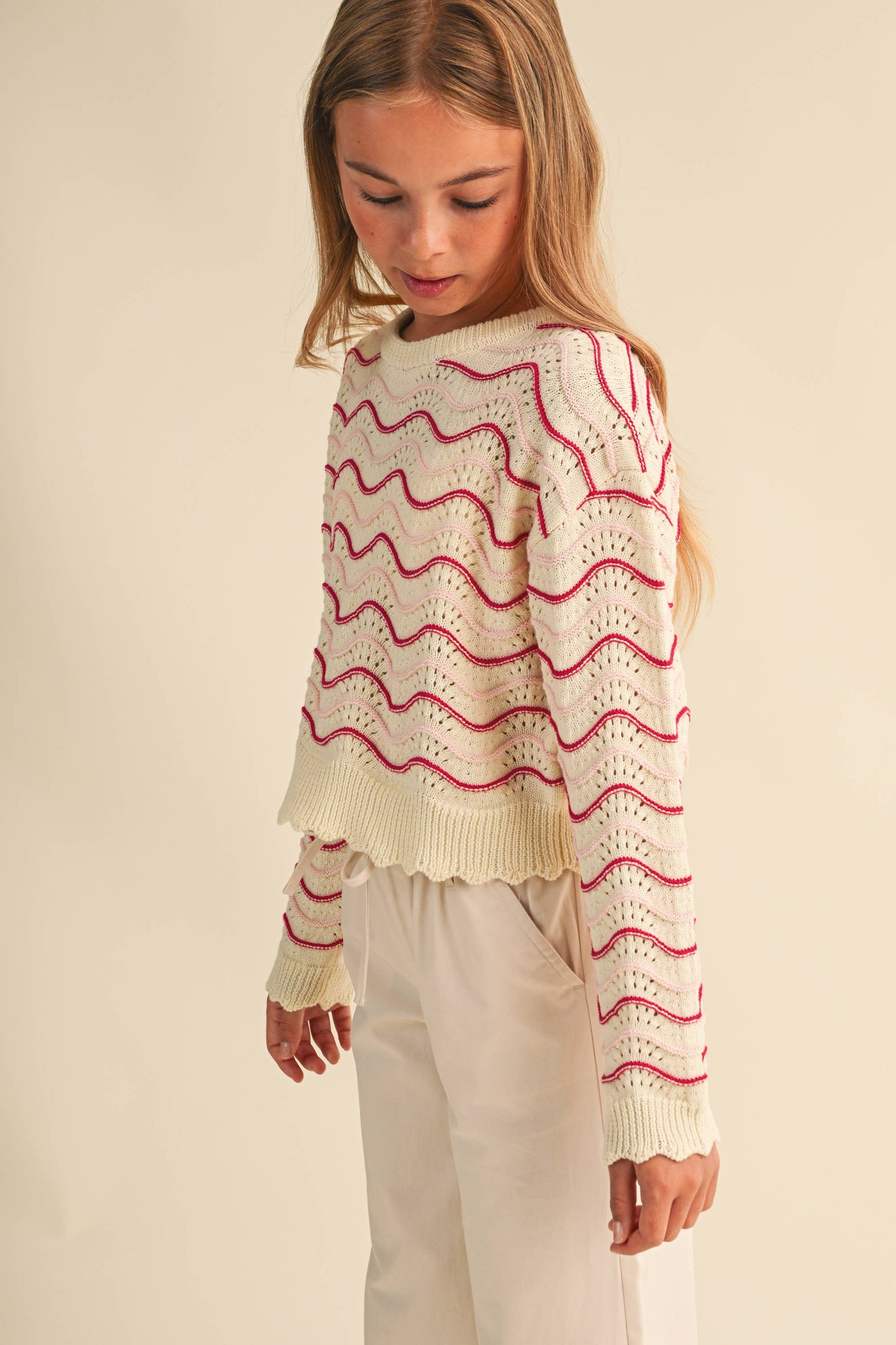 A young girl wearing a cream-colored knit sweater with pink wavy stripes 