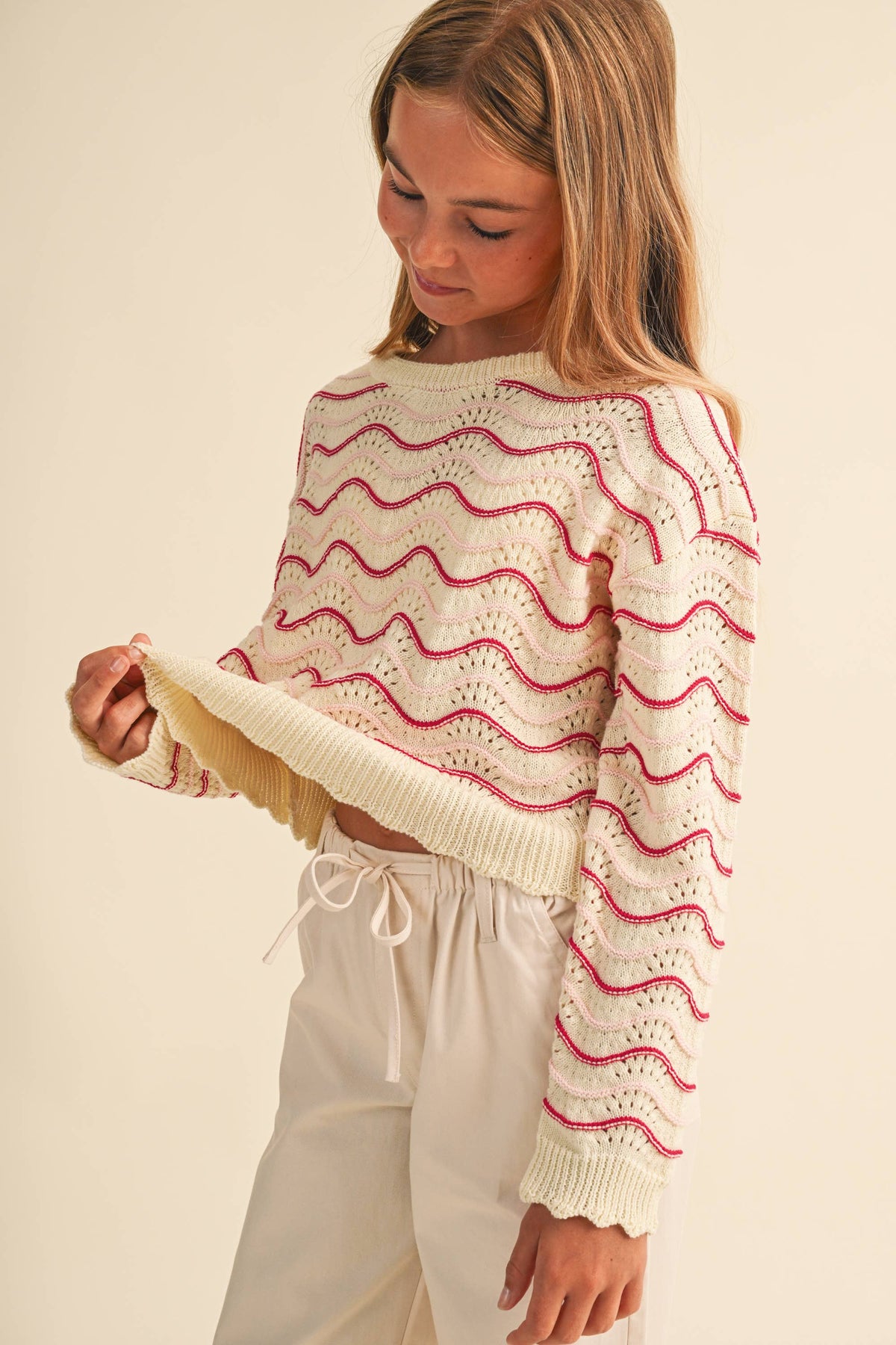 A young girl wearing a cream-colored knit sweater with pink wavy stripes