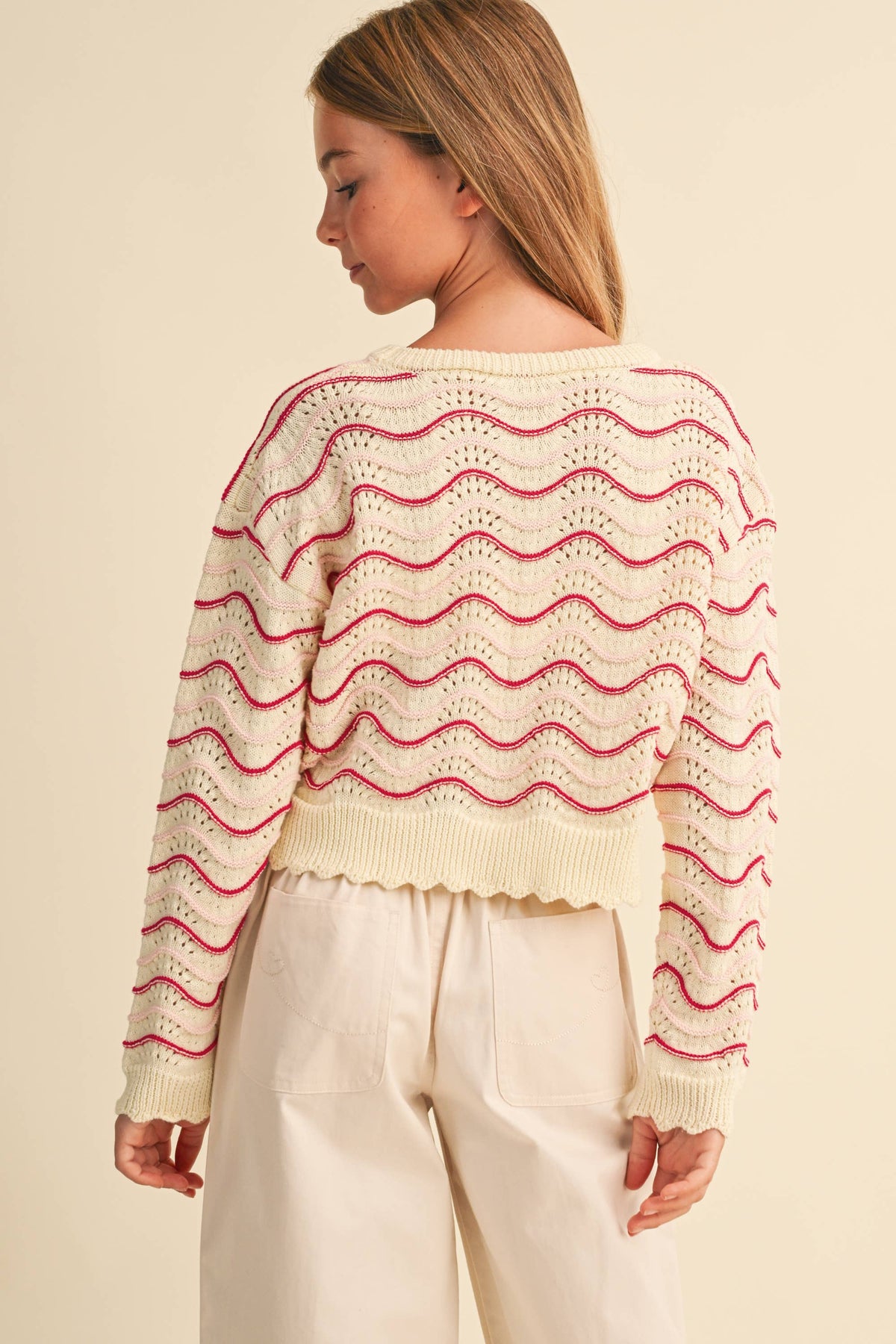 A girl shown from the back wearing a cream-colored knit sweater with pink wavy horizontal stripes 