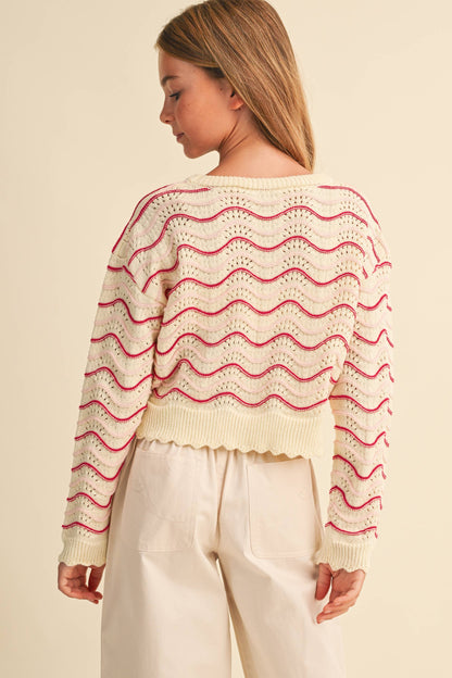 A girl shown from the back wearing a cream-colored knit sweater with pink wavy horizontal stripes 