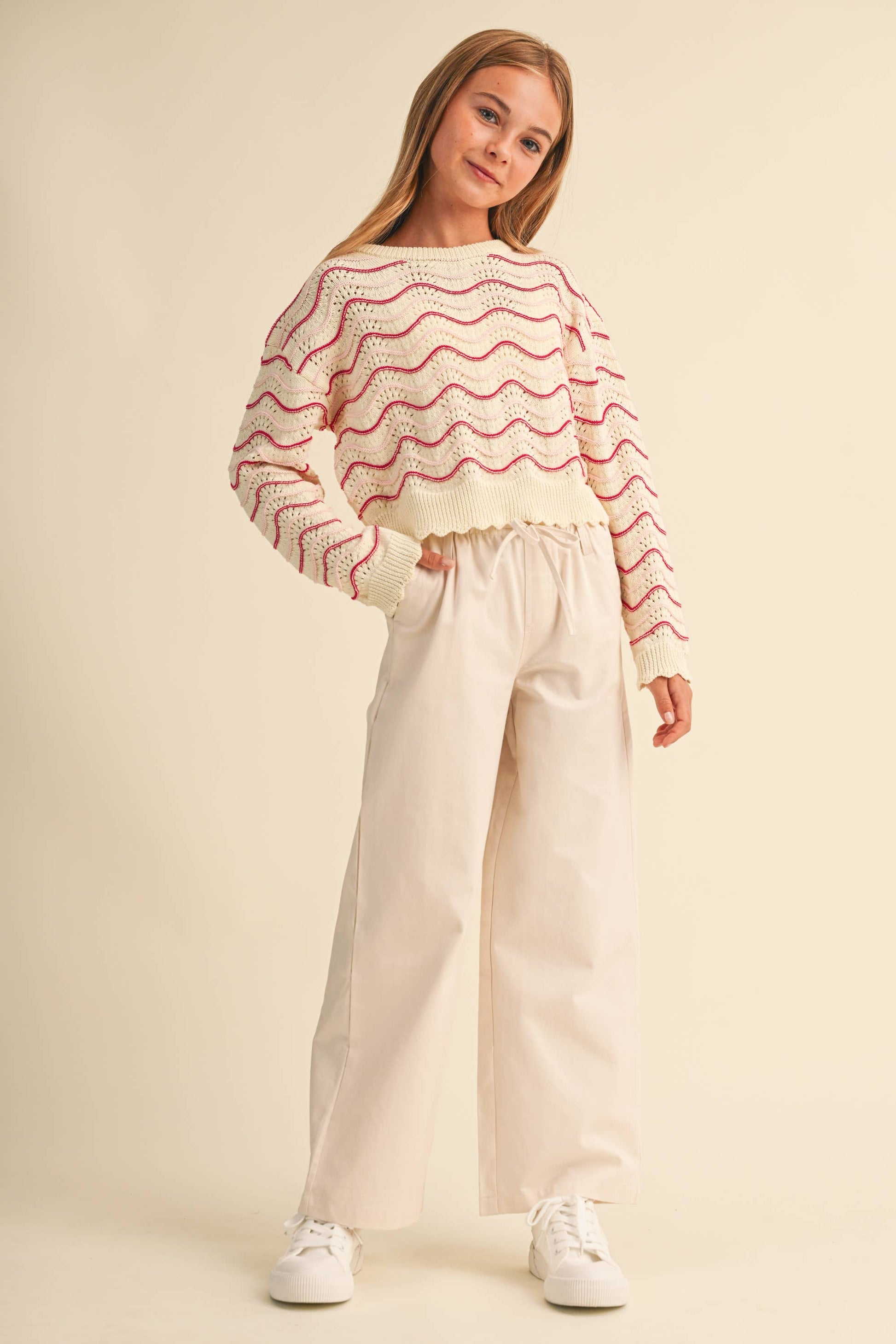 A young girl modeling a cream knit sweater with pink wavy stripes