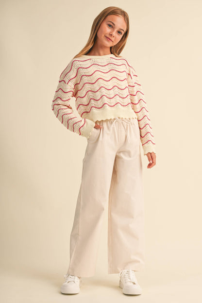 A young girl modeling a cream knit sweater with pink wavy stripes